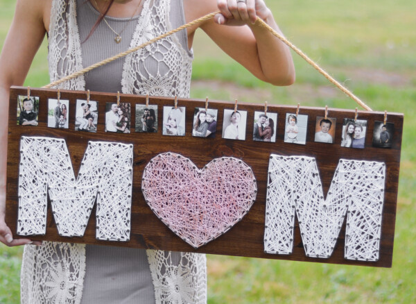 Girl holding sign that says "mom" and has photos on it