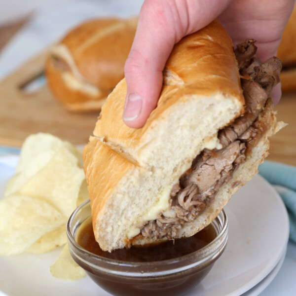 Hand dipping french dip sandwich into au jus