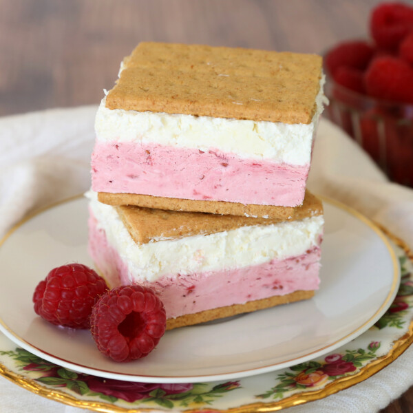 Frozen raspberry cheesecake graham cracker sandwiches on a plate with raspberries