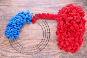 Wire wreath frame on quarter covered with blue loop yarn; a ball of red loop yarn tied to the frame