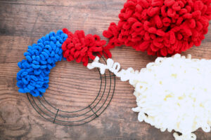 Wire wreath frame wrapped with blue and red loop yarn; white loop yarn tied on