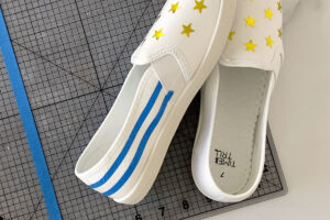 Pair of white canvas shoes with star stickers on the top and rows of masking tape along the back