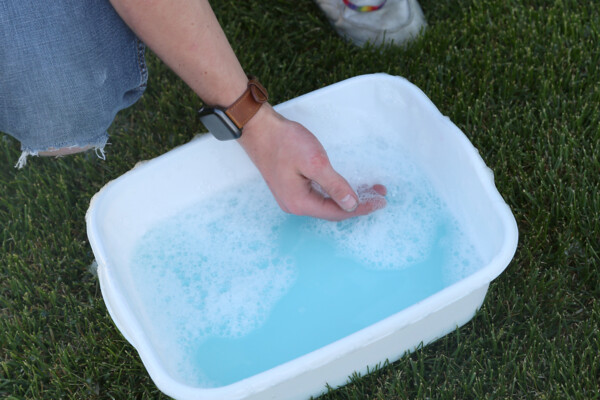 Hand skimming bubbles off top of blue bubble solution