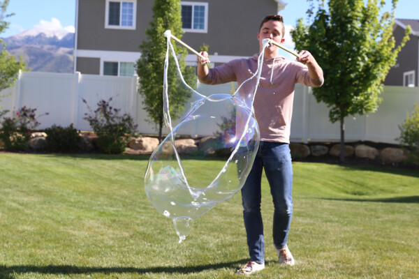 Boy holding DIY bubble wand with sticks opened up to blow bubble