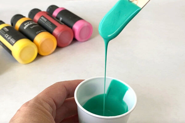 Popsicle stick scooping up paint from a small cup; paint easily runs back into the cup