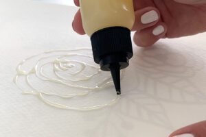 Hand outlining floral design using rubber cement in a small squeeze bottle