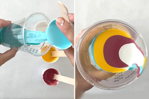 Different colors of paint being carefully poured and layered into a clear cup