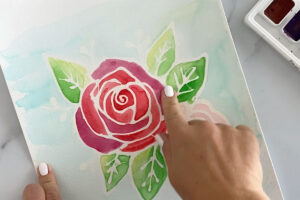Using fingers to rub the rubber cement outline off the floral painting