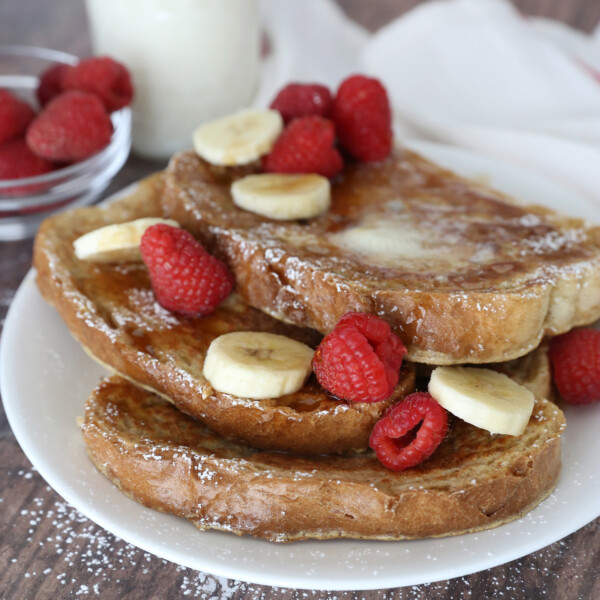 Slices of french toast on a plate with bananas and raspberries