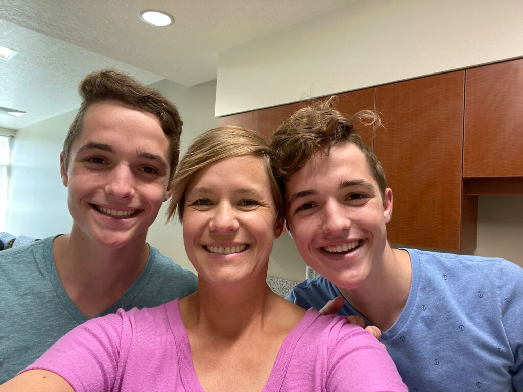 Woman and young adult boys standing in dorm room kitchen