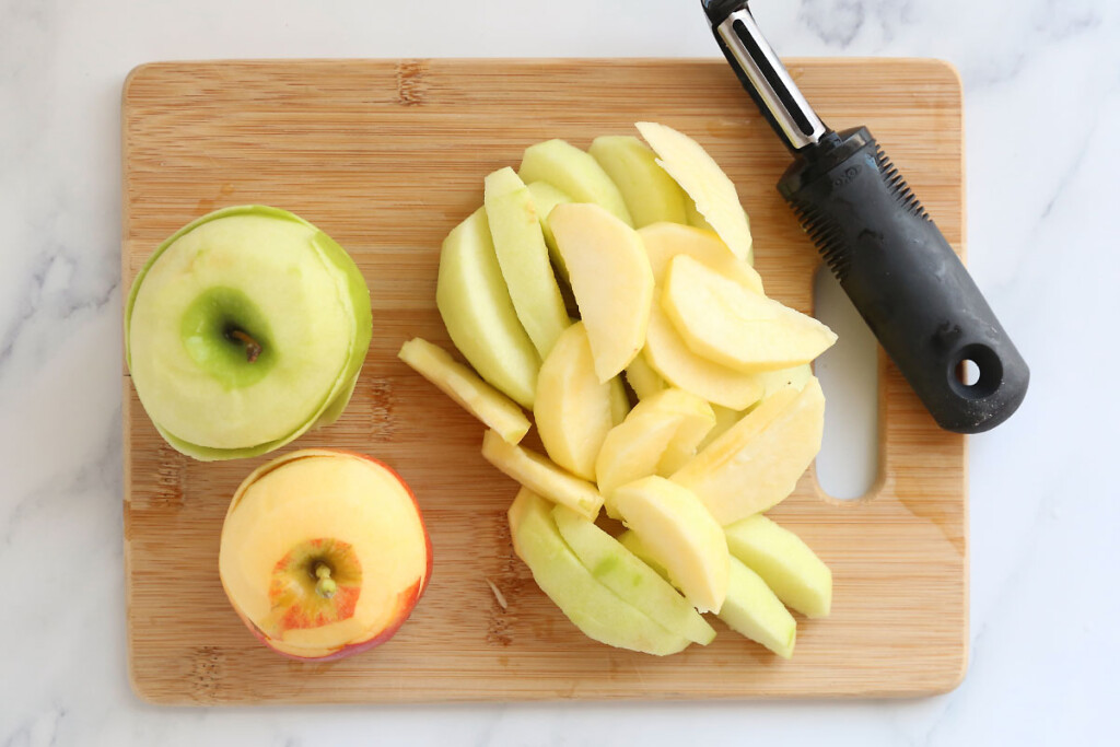 Peeled and sliced apples on a cutting board with peeler