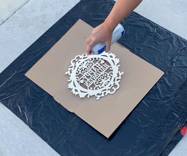 Hand spraying basting spray on the back of a wood Halloween sign