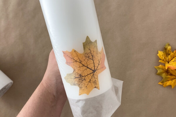 Hand holding wax paper wrapped around candle and leaf