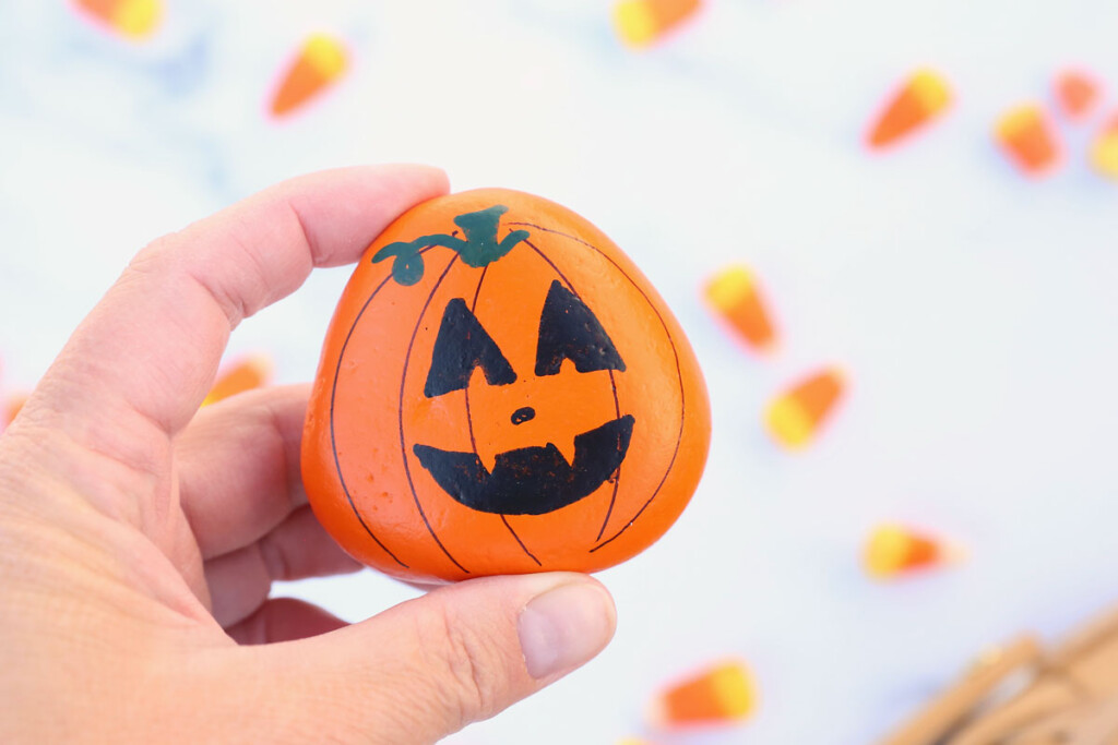 Hand holding a pumpkin painted rock