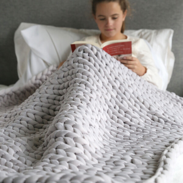 Girl reading a book with a large hand knit blaket