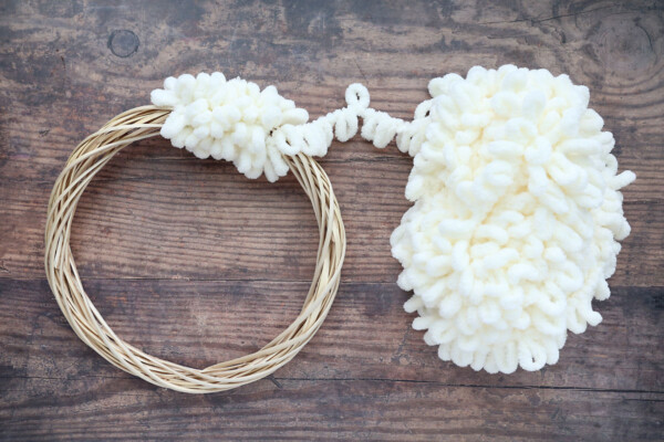Wrapping white loop yarn around a round wreath form