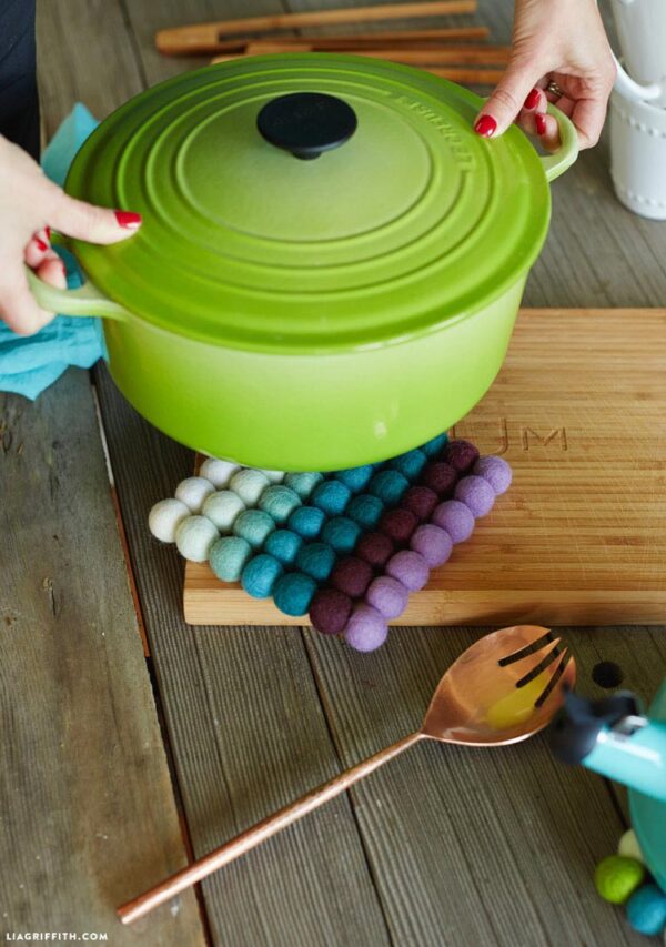 Hands placing large pot on a colorful trivet.