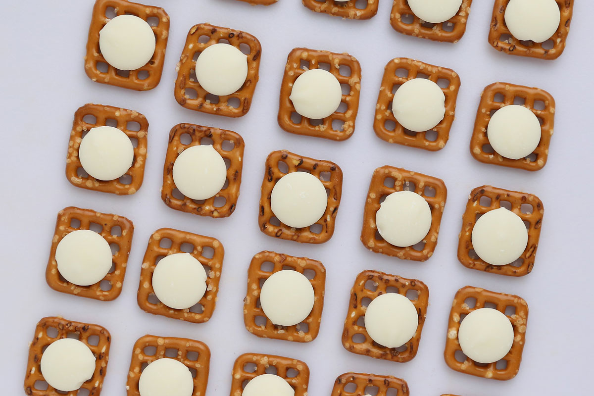 Square pretzels each topped with one white candy melt.