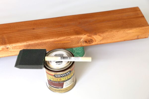 Wood piece propped up on small cup, stain and foam paintbrush.