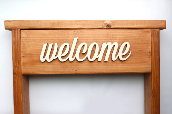 Wooden cutout word "welcome" glued onto front of stand.