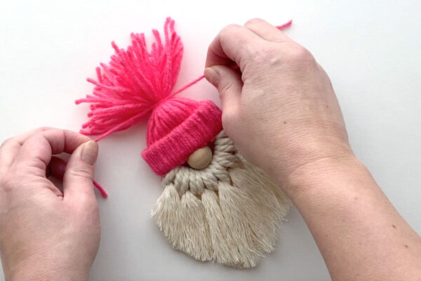 Tying a piece of yarn around the loose yarn at the top of the hat.