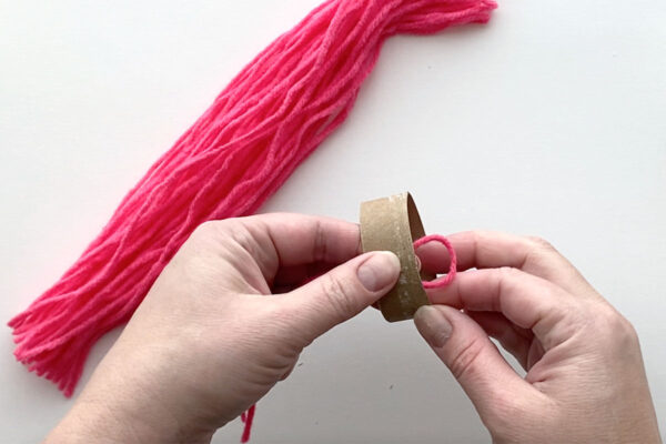 Placing the folded end of a piece of yarn through the cardboard tube.