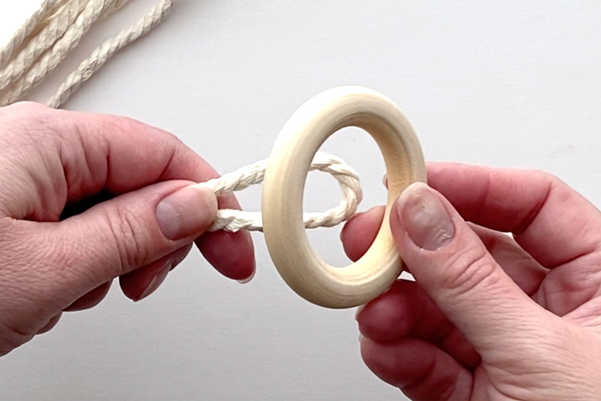 Placing the folded or looped end of macrame cord through the wood ring.