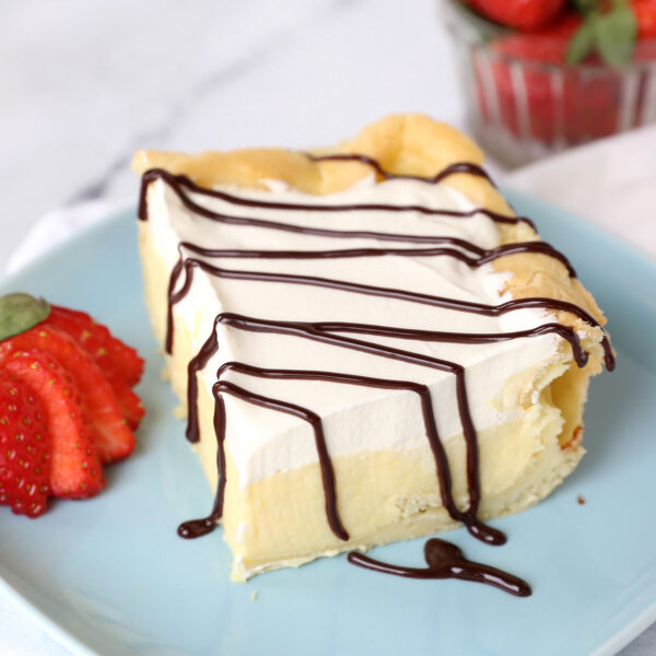 Slice of cream puff cake on a plate with chocolate drizzle and strawberry.