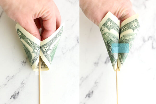 Pulling bottom two corners of bill and pinching them together with fingers; taping them together.