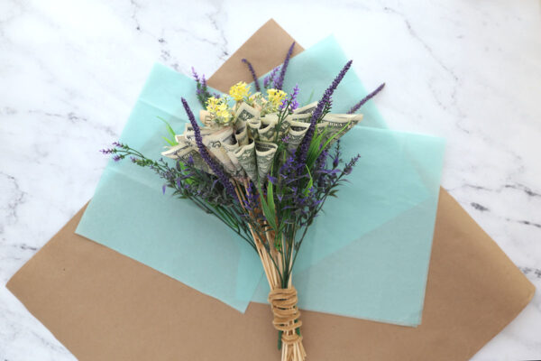 Large piece of kraft paper with squares of tissue paper laid over it; money bouquet laid over the paper.