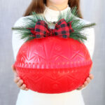 Girl holding giant Christmas ornament.