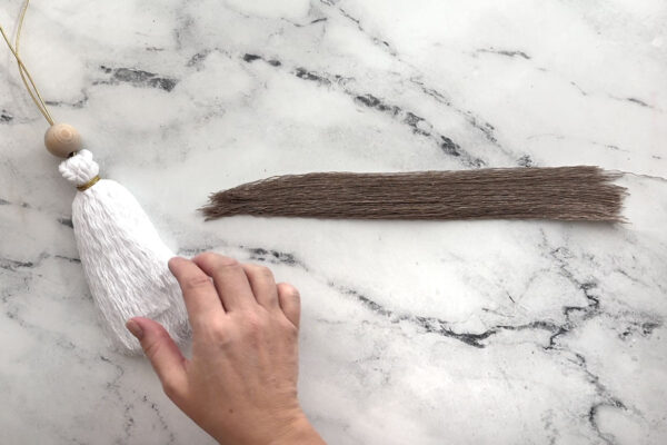 Combing out brown cord to make hair; wood bead added for a head.