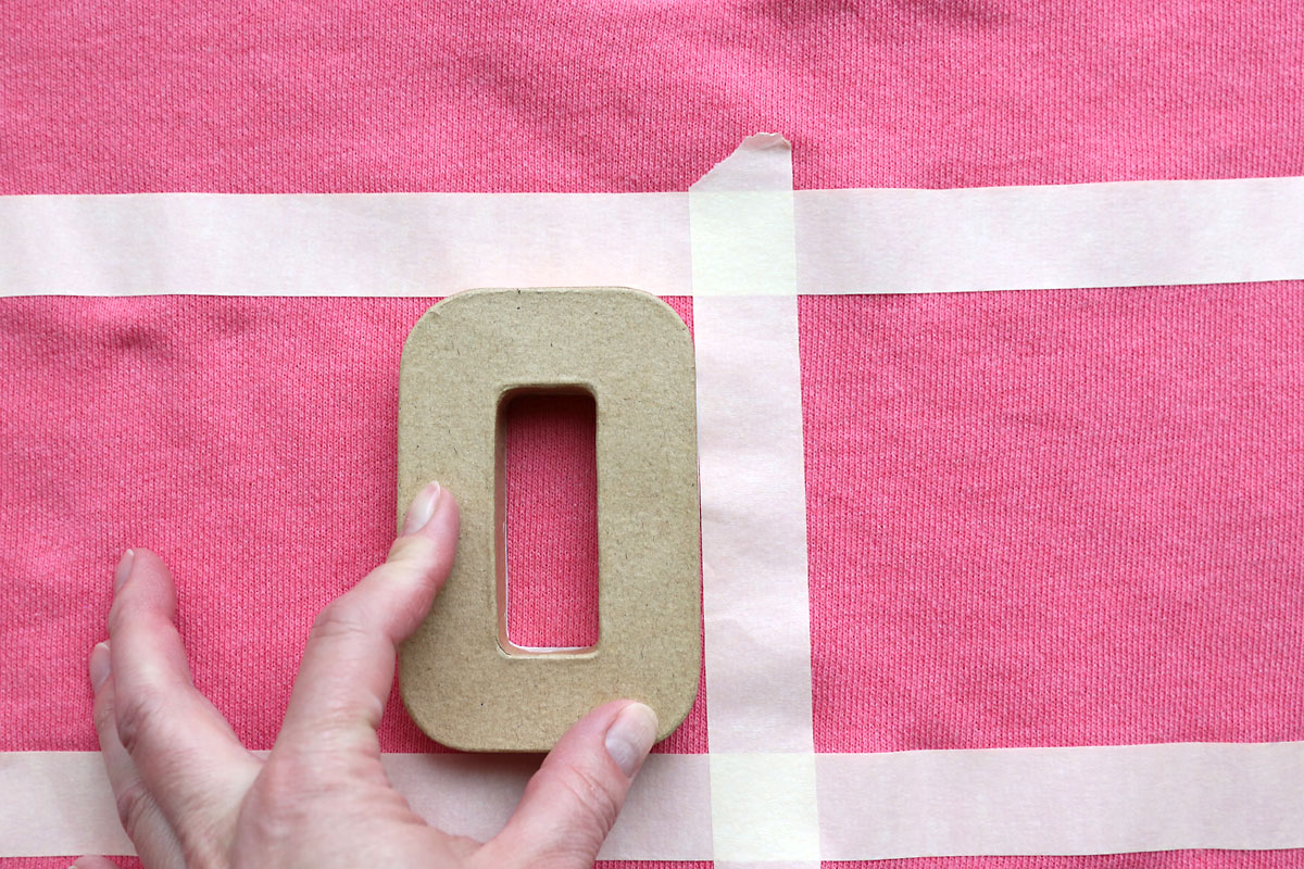 Placing the painted side down to stamp an O on the sweatshirt.