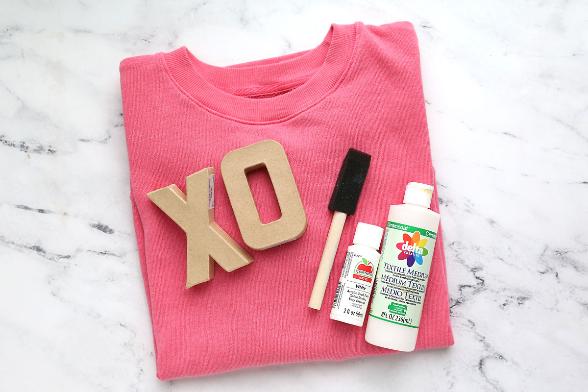 Sweatshirt, X and O paper mache letters, foam paint brush, white paint, textile medium.
