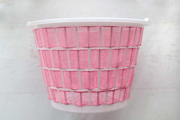 Laundry basket with ribbon woven through all openings on the sides.