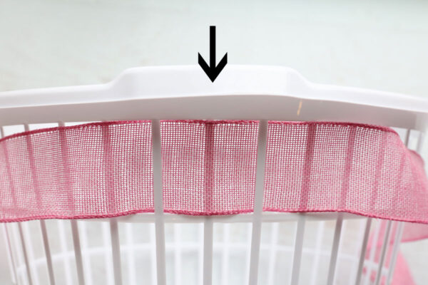 Ribbon woven around laundry basket, making sure it's on the outside of the plastic piece directly in the center below the handle.