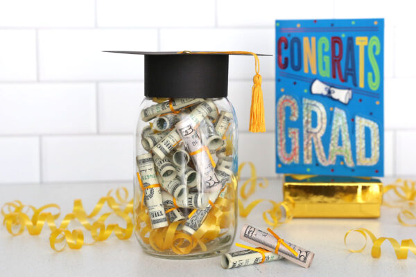 Graduation gift with rolled up money in a mason jar with a grad cap on top.