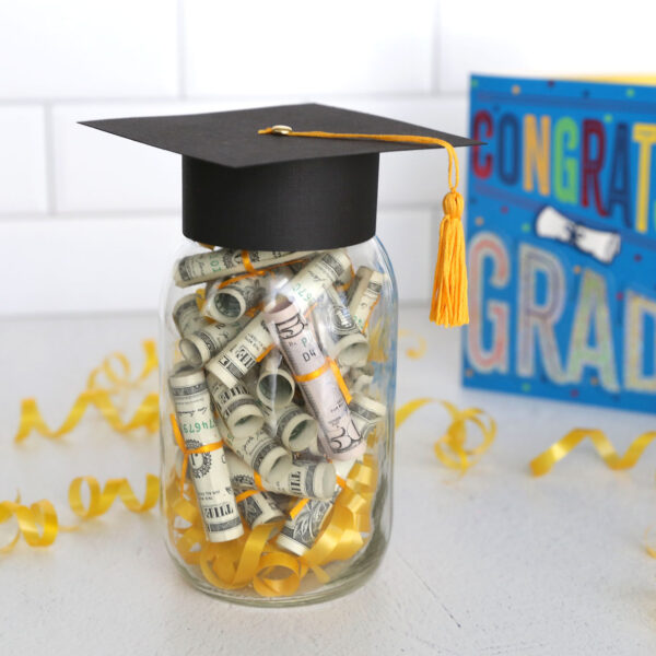 Graduation gift with rolled up money in a mason jar with a grad cap on top.