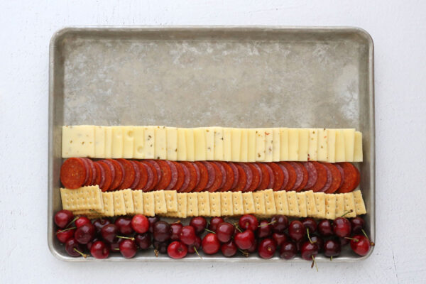 Bottom half of cookie sheet filled with cheese stripe, meat stripe, cracker stripe, cherries stripe.