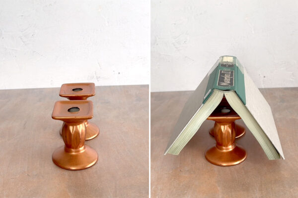Two candle holders, one in front of the other, with a book open on top of them.