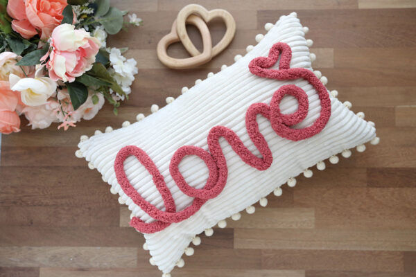 Pillow with the word "love" on it in chunky yarn.