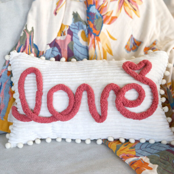 Pillow with the word "love" on it in chunky yarn.