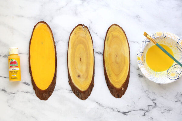 One wood slice painted yellow; two wood slices painted with yellow wash.